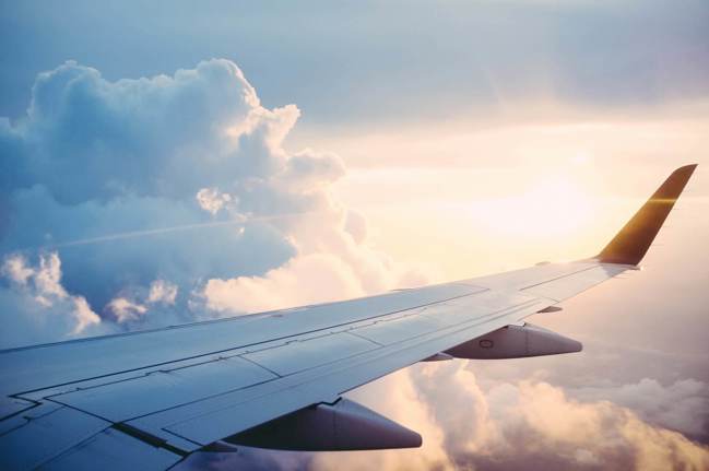 Airplane wing mid flight in the sunshine and clouds