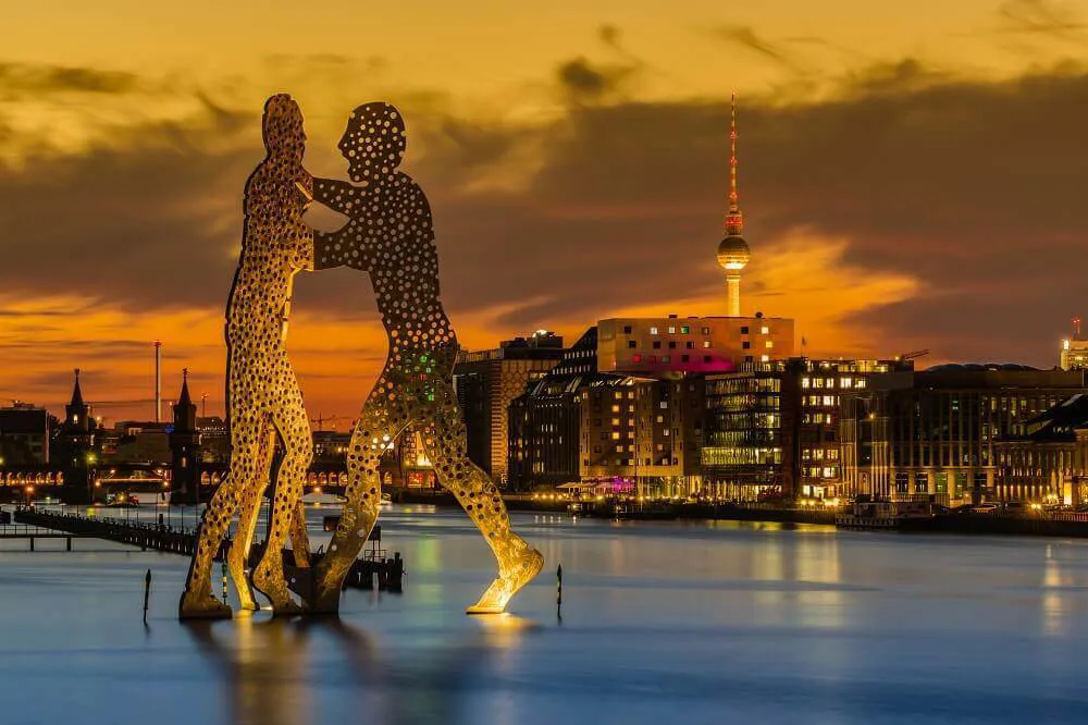 A statue of two people walking towards each other on a backdrop of an illuminated Berlin city at night.