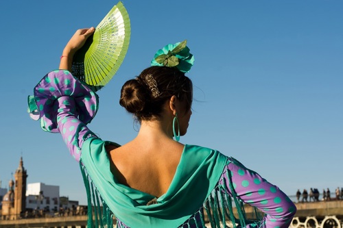 A flamenco dancer in a purple dress with teal polka dots, holding a green fan.