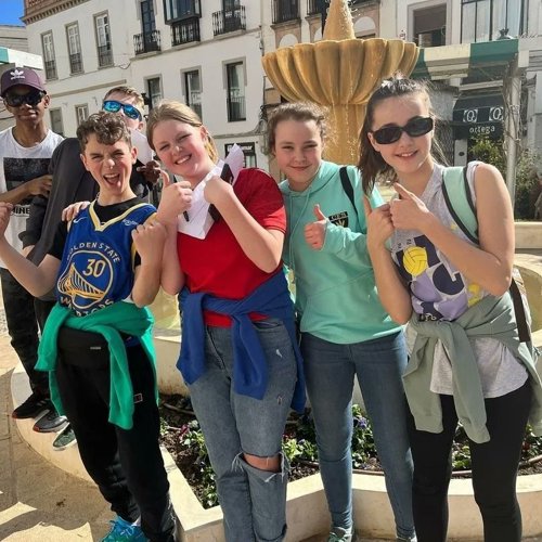 6 students on a recent Spanish language school trip posing in front of a fountain in Spain and giving a thumbs up.