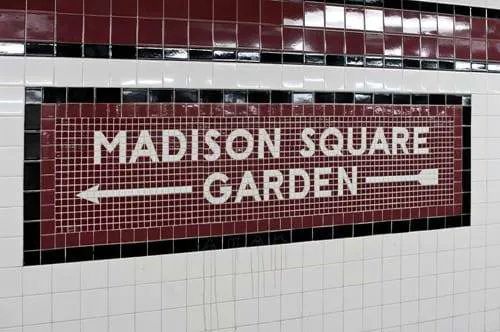 A tiled wall with a sign with an arrow pointing towards Madison Square Garden.