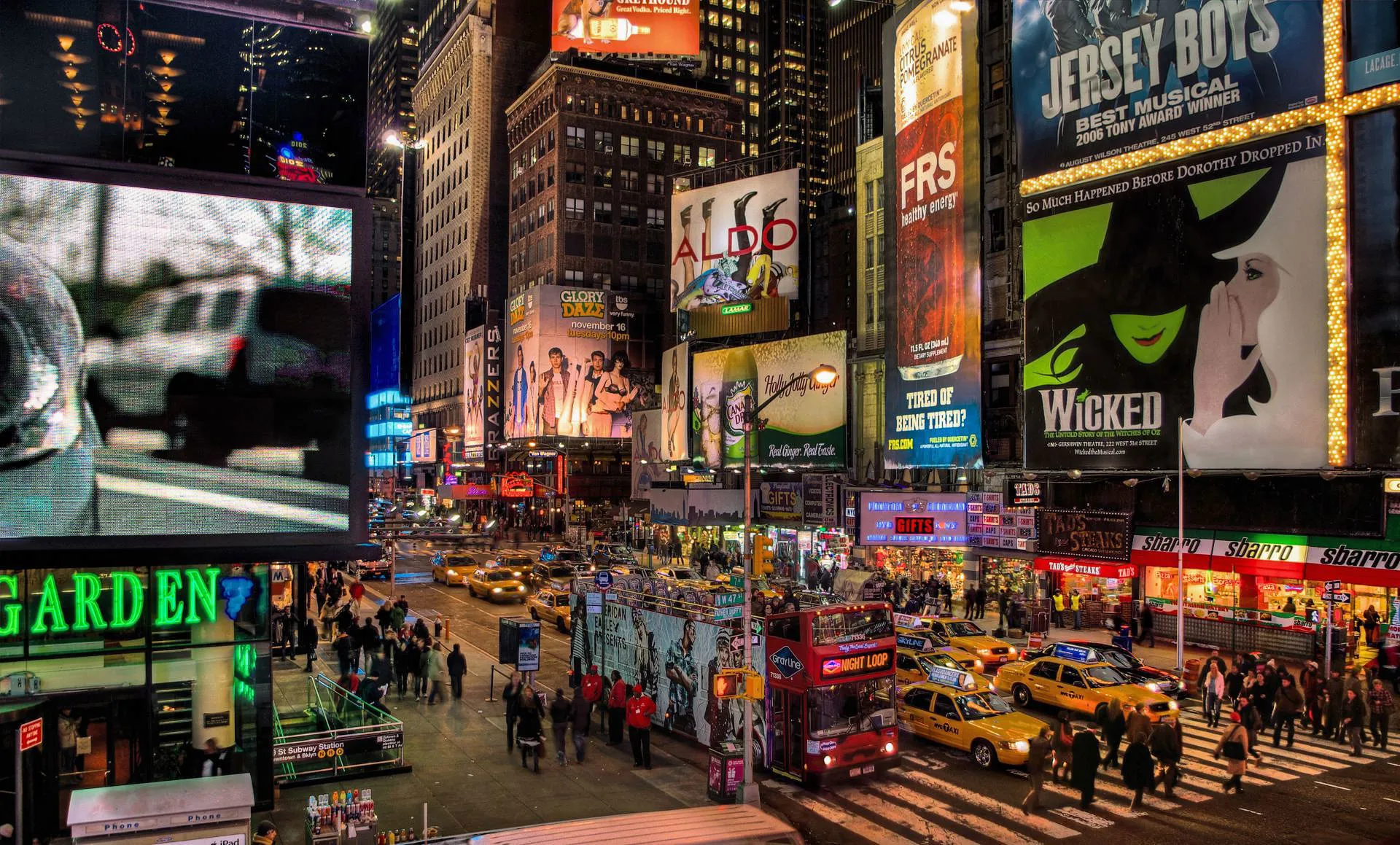 A busy Broadway street with an open top double decker bus, yellow taxis and musical advertisements.