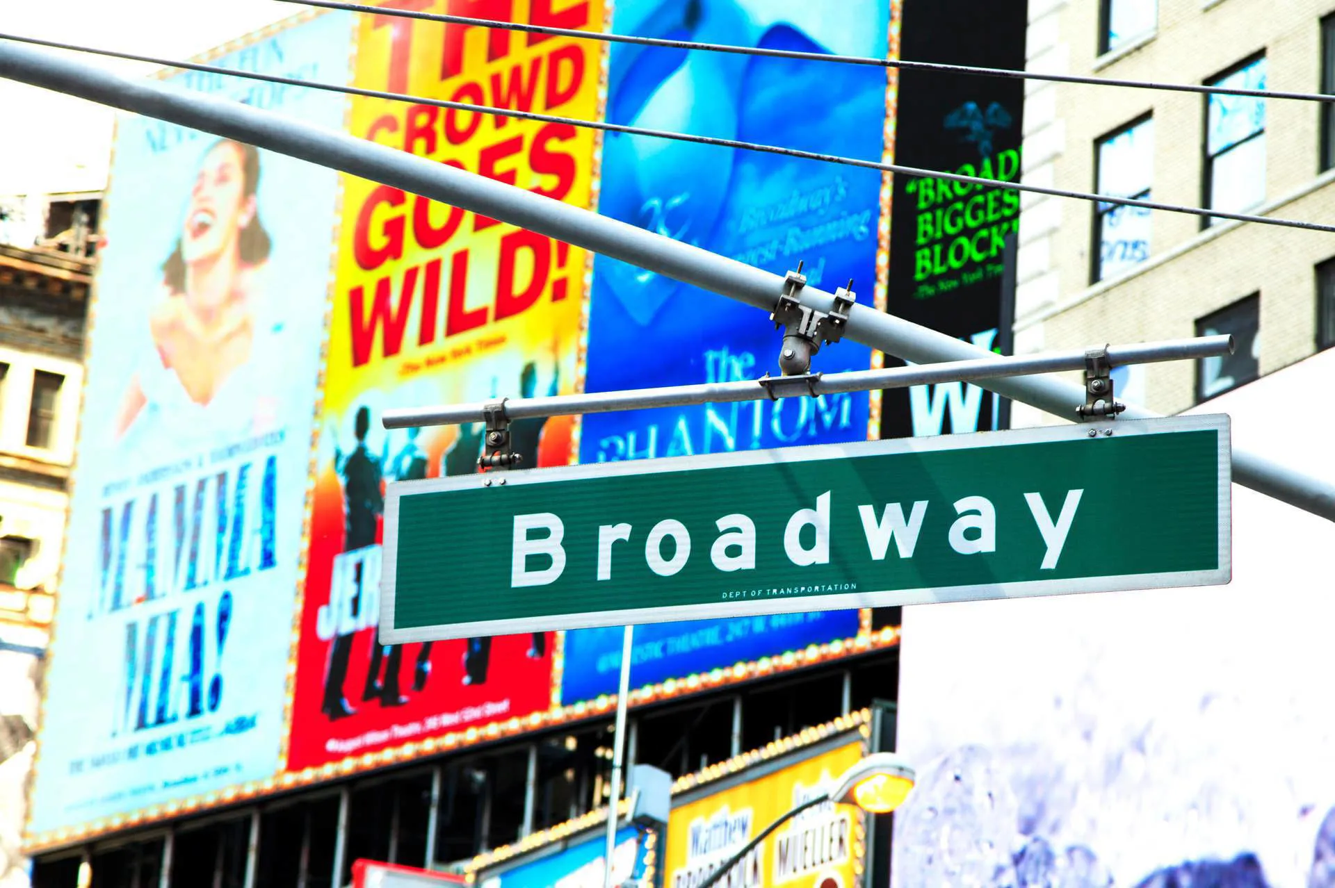 A green Broadway sign with advertisements for Mamma Mia, the Jersey Boys, Wicked and the Phantom of the Opera behind.