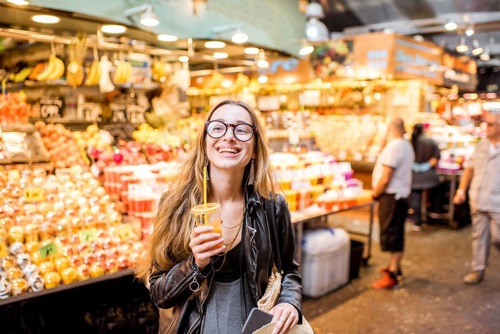 A student smiling in a market in Spain while enjoying a refreshing mango smoothie.